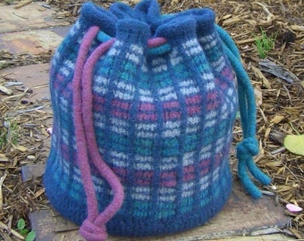 May include: A blue, pink, and white knitted drawstring bag with a plaid pattern. The bag has a long pink drawstring and a shorter blue drawstring.