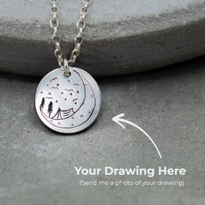 Op de afbeelding: Een zilverkleurige hangerketting met een ronde bedel. De bedel heeft een geëtst ontwerp van een halve maan, sterren, bomen en een tent. De tekst "Your Drawing Here" staat eronder.