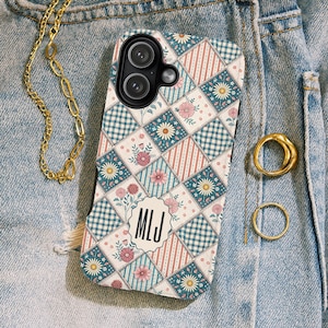 Könnte beinhalten: Eine Handyhülle mit floralem Muster und Patchwork-Design in Türkis, Rosa und Weiß. Die Hülle hat ein Monogramm mit den Initialen "MLJ". Eine goldene Kette und Ringe sind ebenfalls sichtbar.