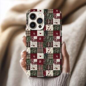 Könnte beinhalten: Eine Handyhülle im Patchwork-Stil mit roten, grünen und cremefarbenen Quadraten. Das Design umfasst Blumenmuster, Schneeflocken und Herzen. Die Hülle wird in einer Hand gehalten, was das detaillierte Design zeigt.