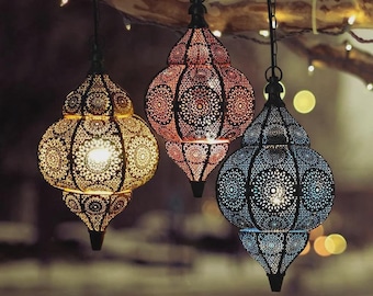 Puede incluir: Tres faroles decorativos colgantes en oro, rojo y azul. Cada farol tiene un diseño de metal calado con forma de lágrima y está suspendido por una cadena. Los faroles están iluminados desde dentro, creando un brillo cálido.