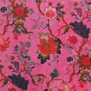 Può includere: Un tessuto rosa acceso con un motivo floreale ripetuto. Il design include grandi fiori stilizzati nei toni del rosso, arancione e bianco, con fogliame verde e blu. I gambi sono marroni, creando un tessuto ricco e colorato.