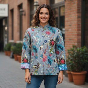 Peut inclure: Veste matelassée grise ornée d'un motif floral bleu, rose et vert. Elle possède un col mandarin, des boutons et des poches. Les poignets présentent un motif bleu et blanc contrastant.