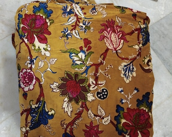 Puede incluir: Tela doblada con fondo amarillo mostaza y estampado floral. El diseño presenta grandes flores en tonos rojos, rosas y burdeos, con detalles azules y blancos. La tela se utiliza probablemente para la decoración del hogar o la ropa.