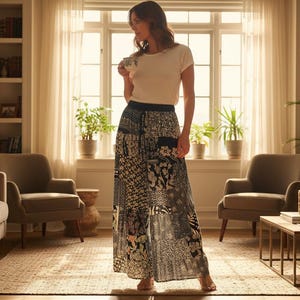 Puede incluir: Una persona con una camiseta blanca y una falda larga estampada en un salón luminoso. La falda presenta un diseño de patchwork con estampados florales y geométricos en negro, blanco y beige. La habitación tiene tonos neutros y luz natural.