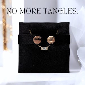 May include: A jewelry set on a black velvet display. The set includes a necklace with a rectangular pendant and matching stud earrings. The earrings and necklace are gold-toned. The text "NO MORE TANGLES" is at the top of the image.