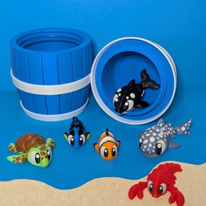 May include: A blue barrel-shaped container with a white rim and a lid, alongside several cartoon sea creatures. The creatures include a turtle, a clownfish, a whale shark, a lobster, a blue tang, and a killer whale.