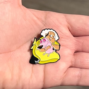 May include: Enamel pin featuring Courage the Cowardly Dog and Muriel Bagge from the animated series. The pin shows Muriel in a yellow dress hugging Courage, who is pink. The pin has black, yellow, pink, brown, and white colors.