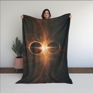 May include: A dark blanket featuring a vibrant, abstract design of two overlapping circles with a bright orange and yellow light burst in the center. The blanket has a soft, plush appearance and is likely made of a comfortable material.