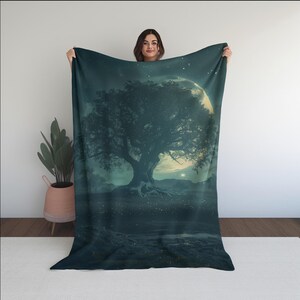 Puede incluir: Una manta de color verde azulado oscuro que presenta un paisaje de fantasía con un gran árbol, una luna llena y un cielo estrellado. El árbol tiene raíces prominentes y una copa completa. La manta es sostenida por una persona.