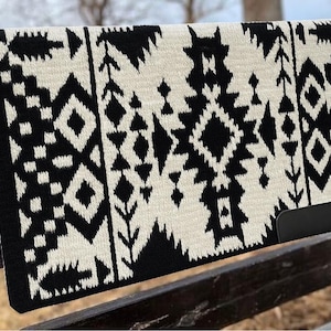 Könnte beinhalten: Eine schwarze und cremefarbene Satteldecke mit geometrischem Muster. Die Decke weist ein sich wiederholendes Design aus Rauten, Dreiecken und anderen Formen auf. Die Decke ist rechteckig und scheint aus einem gewebten Material zu bestehen.