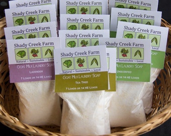 May include: A wicker basket filled with white laundry soap sachets. Each sachet has a label that reads "Shady Creek Farm Goat Milk Laundry Soap" with different scents, including Lavender, Tea Tree, and Unscented. The labels also state "Natural - Sustainable - Local" and indicate the number of loads per sachet.