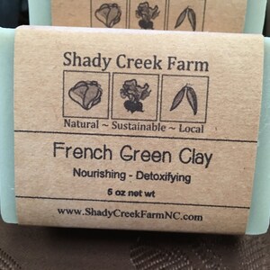 May include: A light green bar of soap with a brown paper label. The label reads "Shady Creek Farm" and "French Green Clay." The soap is 5 oz net weight. The label also states "Natural ~ Sustainable ~ Local."