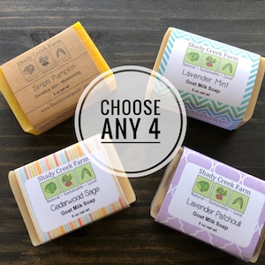 May include: Four bars of goat milk soap with different scents: Simply Pumpkin, Lavender Mint, Cedarwood Sage, and Lavender Patchouli. Each bar is wrapped in colorful paper with a label that includes the name of the scent, the words "Shady Creek Farm", and "Natural - Sustainable - Local". The bars are arranged on a wooden surface. The text "CHOOSE ANY 4" is written in a circle in the center of the image.