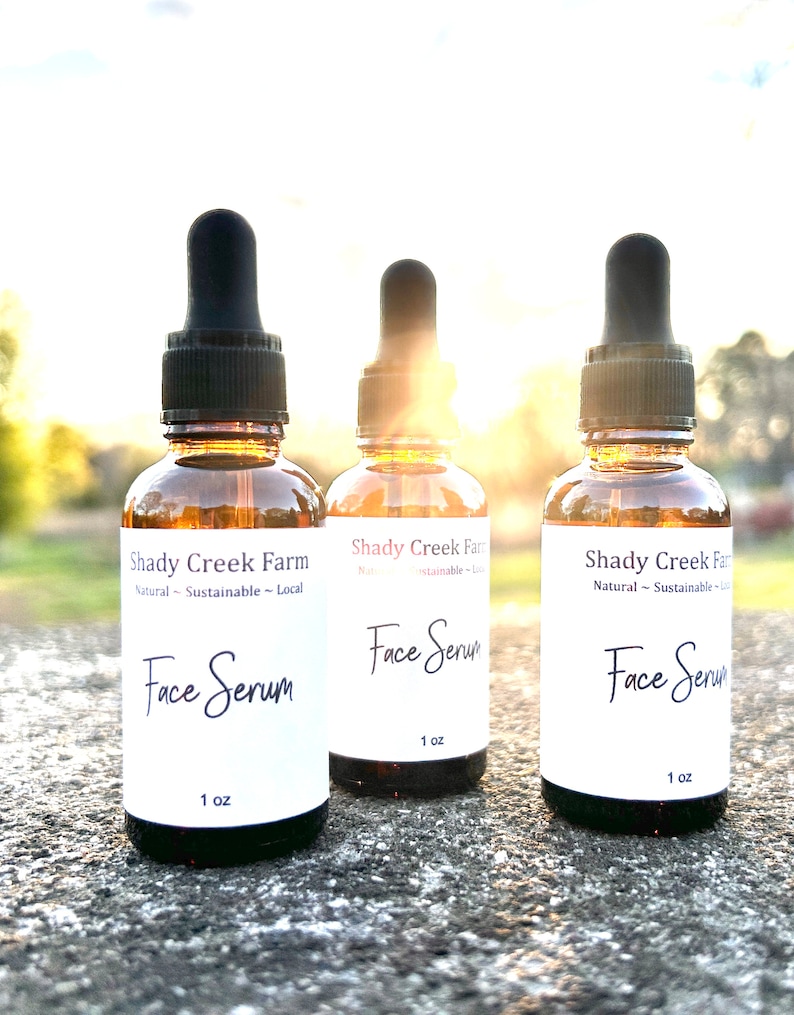 amber glass dropper bottle with white label that reads Face Serum 1 oz. Bottles are sitting outside on concrete table with sun in background shining through bottles with a glowing hue.