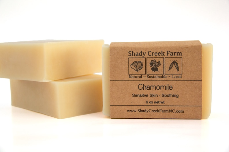 Peut inclure: Deux savons &agrave; la camomille naturels, durables et locaux de Shady Creek Farm. Le savon est con&ccedil;u pour les peaux sensibles et est apaisant. L'&eacute;tiquette est brune avec du texte blanc et des illustrations d'un chou, d'une fleur et d'une feuille. Le savon p&egrave;se 5 onces.