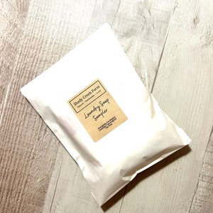 Peut inclure: Un sac en papier blanc avec une &eacute;tiquette brune qui indique "Shady Creek Farm Natural - Sustainable - Local Laundry Soap Sampler Energoing, Eucalyptus Lavender, Lemongrass Tea Tree"