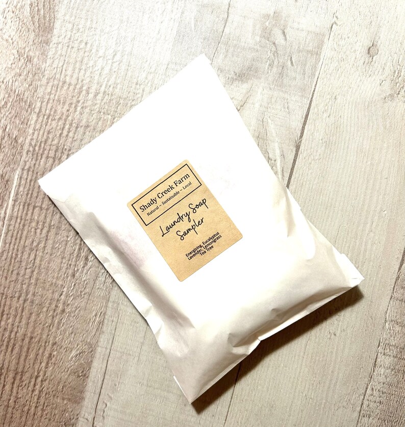 Peut inclure: Un sac en papier blanc avec une &eacute;tiquette brune qui indique "Shady Creek Farm Natural - Sustainable - Local Laundry Soap Sampler Energoing, Eucalyptus Lavender, Lemongrass Tea Tree"