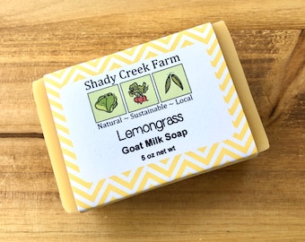 May include: A bar of lemongrass goat milk soap from Shady Creek Farm. The soap is packaged in a yellow and white chevron pattern wrapper with a label that reads "Natural - Sustainable - Local". The label also features illustrations of a head of lettuce, a radish, and a pea pod.