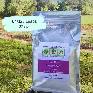 May include: A white resealable bag of goat milk laundry soap with a lavender scent. The bag is labeled "Shady Creek Farm" and states that the soap is natural, sustainable, and local. The bag also states that the soap is good for 64 loads or 128 HE loads. The bag is sitting on a green grassy surface.