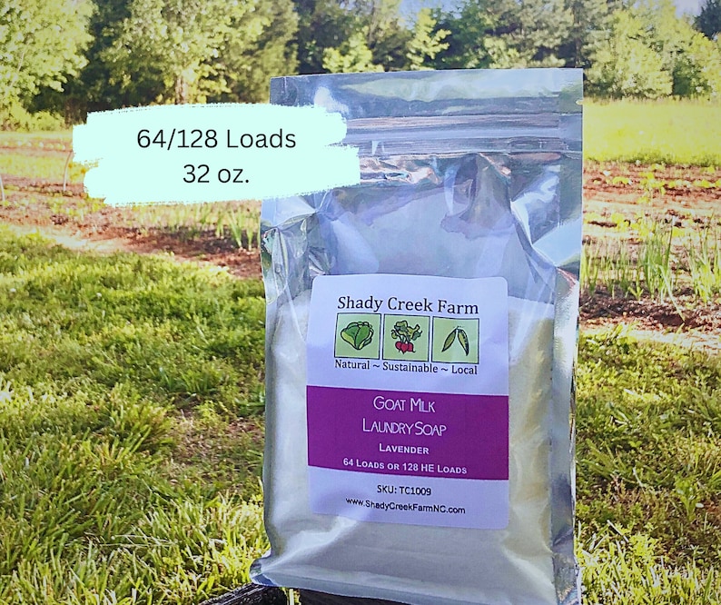 May include: A white resealable bag of goat milk laundry soap with a lavender scent. The bag is labeled "Shady Creek Farm" and states that the soap is natural, sustainable, and local. The bag also states that the soap is good for 64 loads or 128 HE loads. The bag is sitting on a green grassy surface.