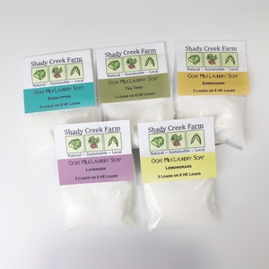 Peut inclure: Cinq petits sachets blancs de savon &agrave; lessive au lait de ch&egrave;vre avec des &eacute;tiquettes indiquant "Shady Creek Farm" et listant diff&eacute;rents parfums : Eucalyptus, Tea Tree, &Eacute;nergisant, Lavande et Citronnelle. Chaque sachet est &eacute;tiquet&eacute; "Naturel - Durable - Local" et indique le nombre de brass&eacute;es que le savon fera.