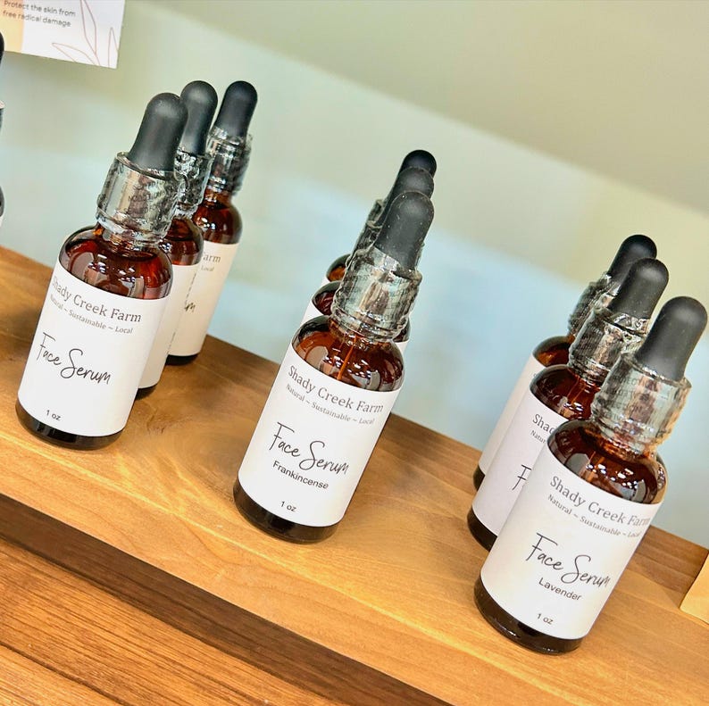 May include: A shelf display of small brown glass bottles with dropper tops. Each bottle is labeled "Shady Creek Farm Face Serum" with a different scent: Frankincense and Lavender. The bottles are 1 oz each.