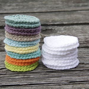 Peut inclure: Une pile de ronds en coton crochet&eacute;s de couleurs, avec une pile de ronds en coton crochet&eacute;s blancs &agrave; c&ocirc;t&eacute;. Les deux piles sont sur une surface en bois.