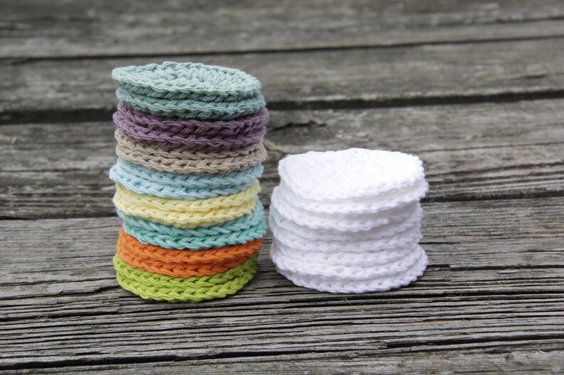 Peut inclure: Une pile de ronds en coton crochet&eacute;s de couleurs, avec une pile de ronds en coton crochet&eacute;s blancs &agrave; c&ocirc;t&eacute;. Les deux piles sont sur une surface en bois.