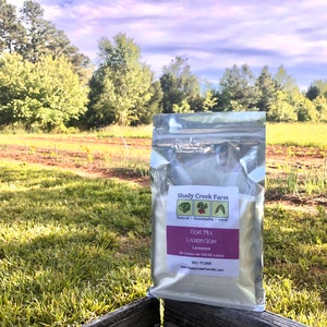 May include: A silver resealable pouch of goat milk laundry soap with a lavender scent. The pouch is labeled "Shady Creek Farm" and features a logo with a leaf, a strawberry, and a cabbage. The text on the pouch reads "Natural - Sustainable - Local" and "Goat Milk Laundry Soap Lavender 54 Loads or 1.25 kg Loads SKU TC1009 www.ShadyCreekFarm.com".