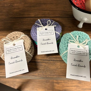 Peut inclure: Trois ensembles de disques faciaux r&eacute;utilisables en coton crochet&eacute; beige, violet et turquoise. Chaque ensemble est li&eacute; avec un ruban blanc et comprend une &eacute;tiquette blanche avec le texte "Shady Creek Farm" et "Disques faciaux r&eacute;utilisables" imprim&eacute; dessus.