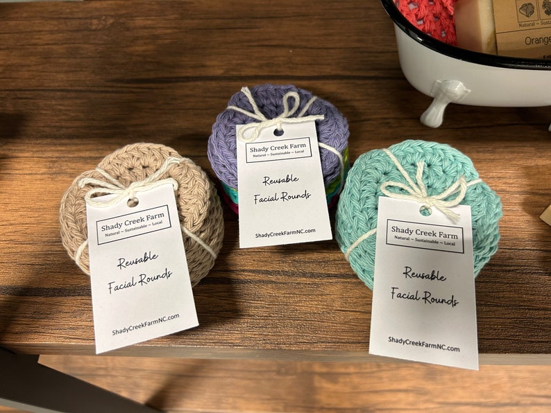 Peut inclure: Trois ensembles de disques faciaux r&eacute;utilisables en coton crochet&eacute; beige, violet et turquoise. Chaque ensemble est li&eacute; avec un ruban blanc et comprend une &eacute;tiquette blanche avec le texte "Shady Creek Farm" et "Disques faciaux r&eacute;utilisables" imprim&eacute; dessus.