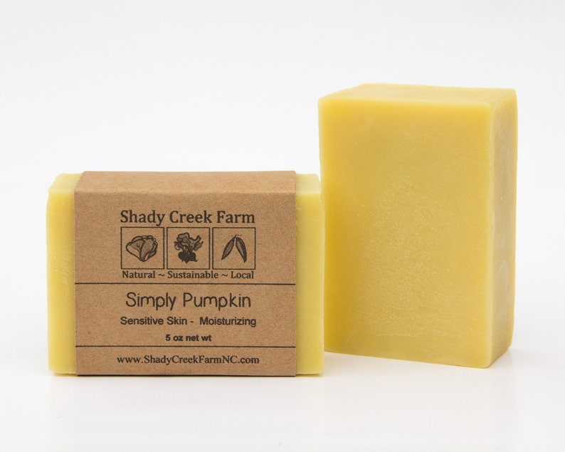 May include: A bar of yellow soap with a brown paper label that reads "Shady Creek Farm" with a logo of three icons representing natural, sustainable, and local. The label also reads "Simply Pumpkin", "Sensitive Skin - Moisturizing", "5 oz net wt", and "www.ShadyCreekFarmNC.com".