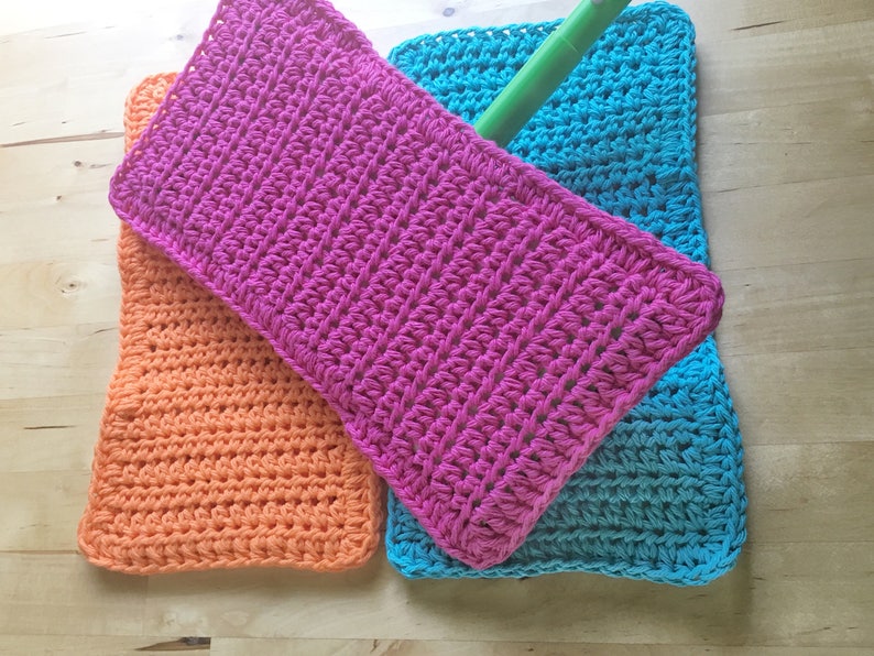 May include: Three crocheted mop heads in pink, orange, and blue. The mop heads are made with a thick yarn and have a textured surface.
