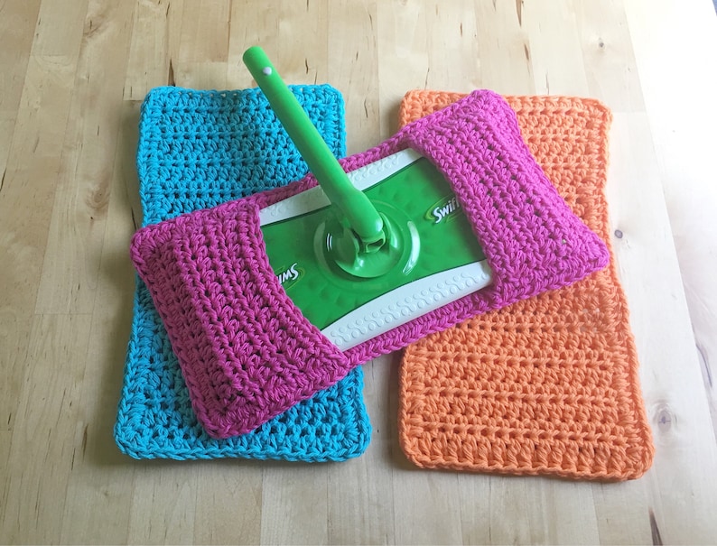 May include: Three crocheted mop head covers in pink, turquoise, and orange. The covers are made with a simple stitch pattern and have a pocket to hold the mop head.