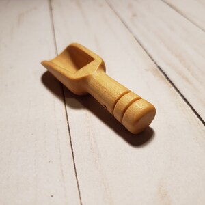 May include: A small wooden scoop with a rounded handle. The scoop is light brown and has a smooth finish.