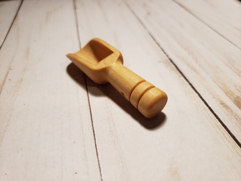 May include: A small wooden scoop with a rounded handle. The scoop is light brown and has a smooth finish.