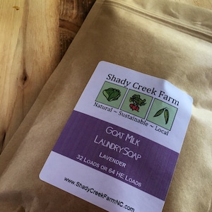 May include: A brown paper pouch containing goat milk laundry soap with a lavender scent. The label reads Shady Creek Farm, Natural ~ Sustainable ~ Local, Goat Milk Laundry Soap, Lavender, 32 Loads or 64 HE Loads, and www.ShadyCreekFarmNC.com.