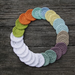 Peut inclure: Un cercle de rondes en coton crochet&eacute;es de diff&eacute;rentes couleurs, dont le blanc, le vert, le bleu et l'orange. Les rondes sont dispos&eacute;es en arc-en-ciel sur une surface en bois.