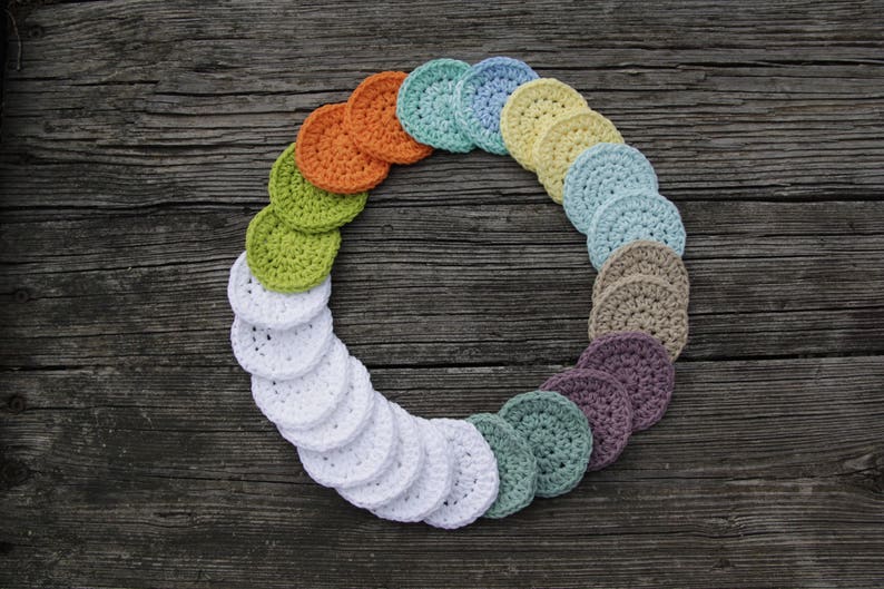 Peut inclure: Un cercle de rondes en coton crochet&eacute;es de diff&eacute;rentes couleurs, dont le blanc, le vert, le bleu et l'orange. Les rondes sont dispos&eacute;es en arc-en-ciel sur une surface en bois.