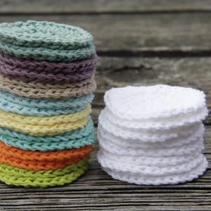 Peut inclure: Une pile de 10 disques de d&eacute;maquillant en coton crochet&eacute;s ronds de diff&eacute;rentes couleurs, dont le vert, le jaune, l'orange et le bleu, &agrave; c&ocirc;t&eacute; d'une pile de 7 disques de d&eacute;maquillant en coton crochet&eacute;s blancs.