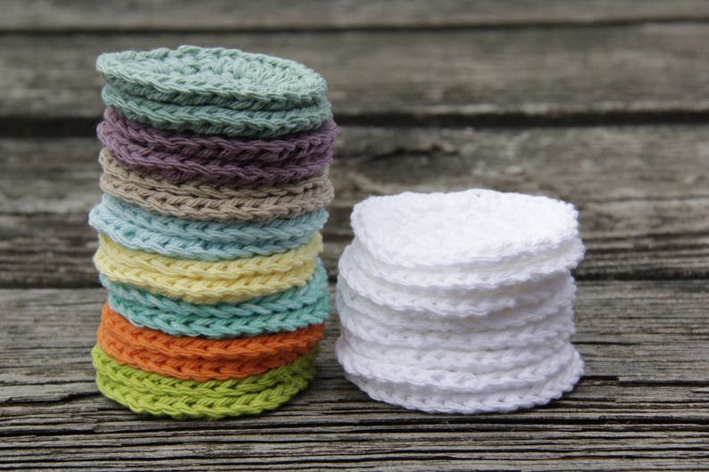 Peut inclure: Une pile de 10 disques de d&eacute;maquillant en coton crochet&eacute;s ronds de diff&eacute;rentes couleurs, dont le vert, le jaune, l'orange et le bleu, &agrave; c&ocirc;t&eacute; d'une pile de 7 disques de d&eacute;maquillant en coton crochet&eacute;s blancs.
