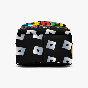 May include: Black backpack with a repeating pattern of white squares. The top of the backpack features colorful text. The backpack is designed for carrying books, supplies, or personal items.