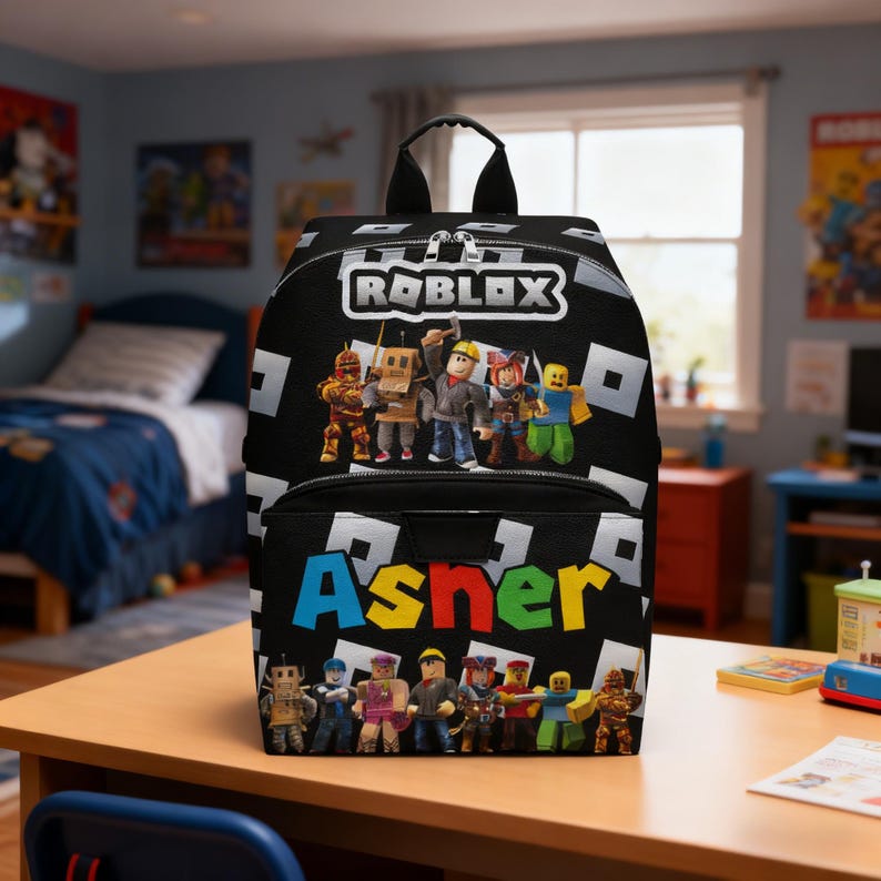 May include: Black backpack featuring the Roblox logo and various character illustrations. The name "Asner" is printed in colorful letters on the front. The backpack has a top handle and a front pocket.