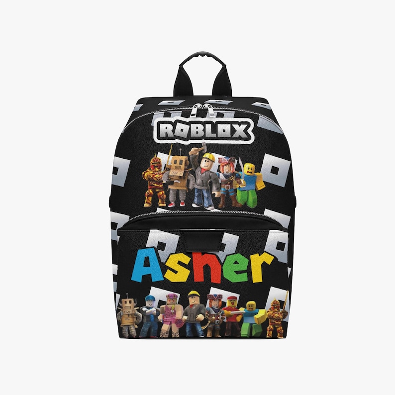 May include: Black backpack featuring the Roblox logo and characters. The name "Asher" is printed in colorful letters on the front. The backpack has a black handle and a black and white pattern.