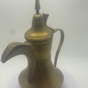 May include: A vintage brass coffee pot with a long spout, curved handle, and a pointed top. The pot has etched floral designs and a decorative finial. The overall design is ornate and traditional.