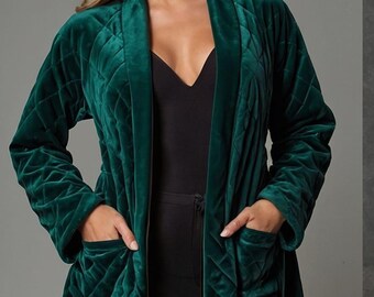 May include: A quilted emerald green velvet robe with a shawl collar and pockets. The robe is long and has a diamond pattern. The model is wearing a black top and trousers. The robe is a luxurious garment.