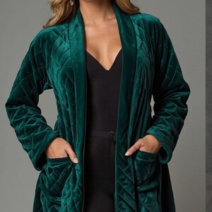 May include: A quilted emerald green velvet robe with a shawl collar and pockets. The robe is long and has a diamond pattern. The model is wearing a black top and trousers. The robe is a luxurious garment.