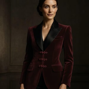 Może przedstawiać: Bordowa aksamitna marynarka z czarnymi satynowymi klapami i trzema ozdobnymi zapięciami żabkowymi. Marynarka ma dwie przednie kieszenie i dopasowany krój, odpowiedni na formalne lub półformalne okazje.