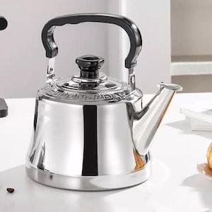 May include: A shiny, stainless steel stovetop kettle with a black handle and lid. The kettle has a decorative band around the top and a spout for pouring. The handle is arched, and the lid has a small, round knob.